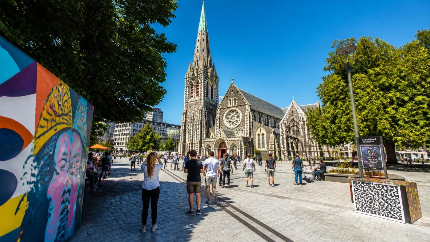 ChristChurch Cathedral and Cathedral Square in Christchurch, New Zealand, with pedestrians and street art nearby.