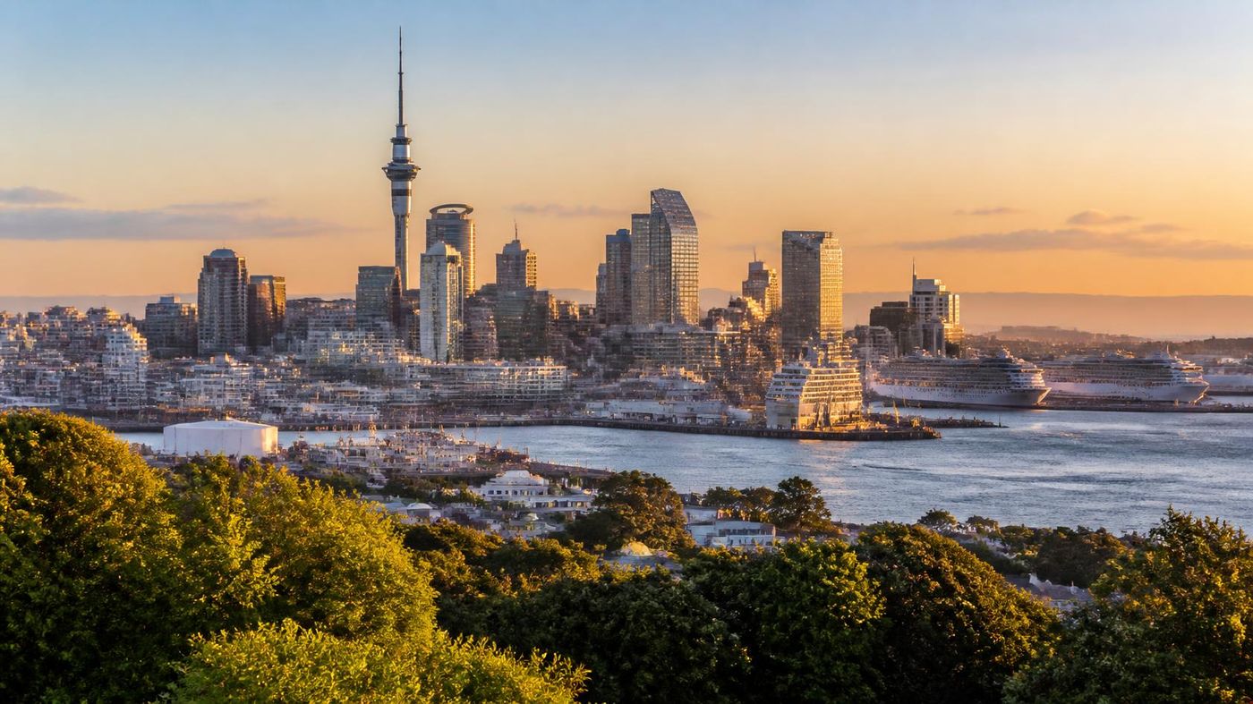 Auckland skyline at sunset featuring the Sky Tower, harbour and cruise ships docked at the waterfront.