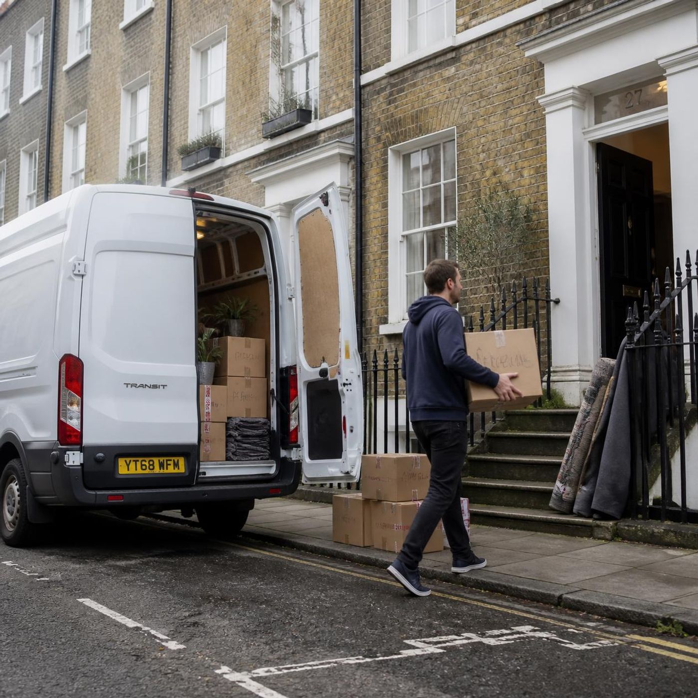 Person carrying a cardboard box from a white delivery van into a London terraced house