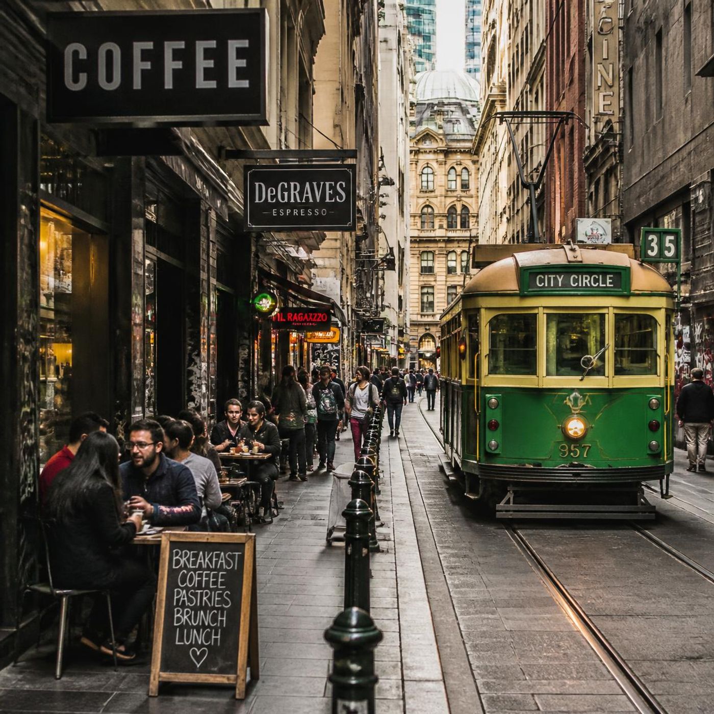 Melbourne laneway with outdoor cafe seating and iconic green and gold tram passing through the narrow street lined with coffee shops
