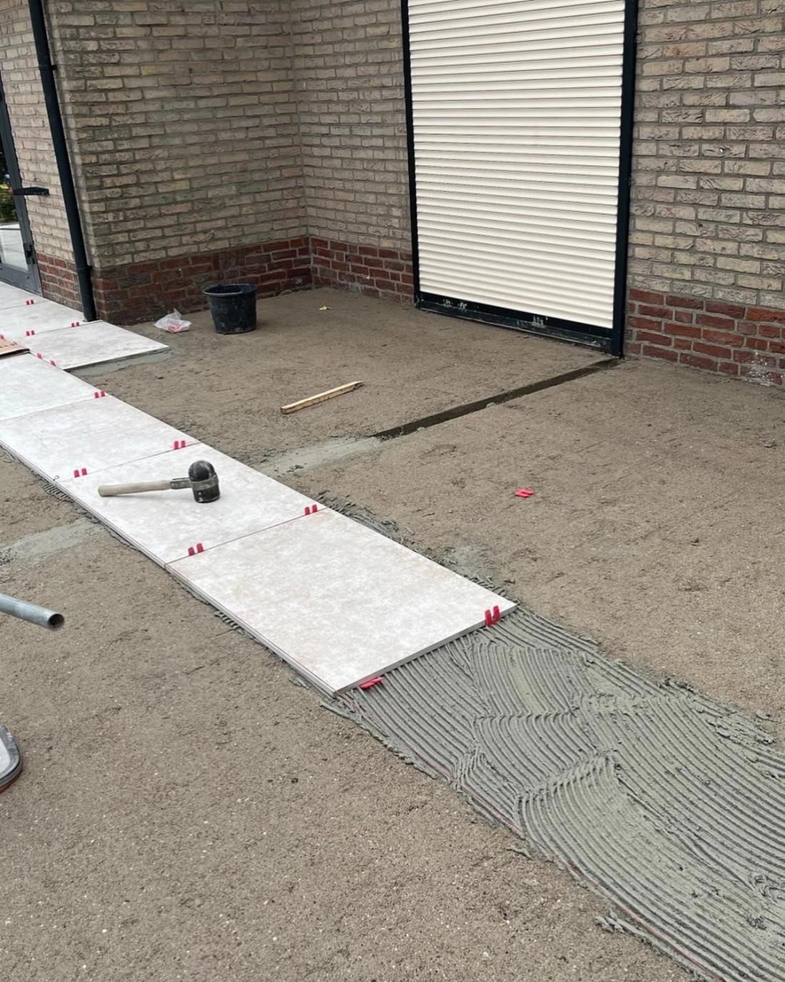 Grote keramische tegels worden met tegelclips op een lijmlaag gelegd