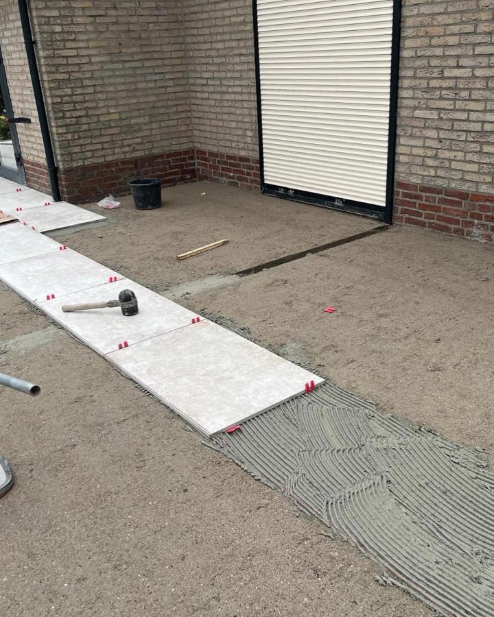 Grote keramische tegels worden met tegelclips op een lijmlaag gelegd
