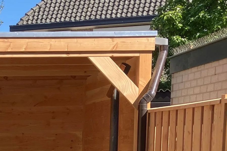 Hoek van de houten overkapping met schoor en regenpijp, met daarnaast de nieuwe houten schutting, in de tuin van Pim in Breda