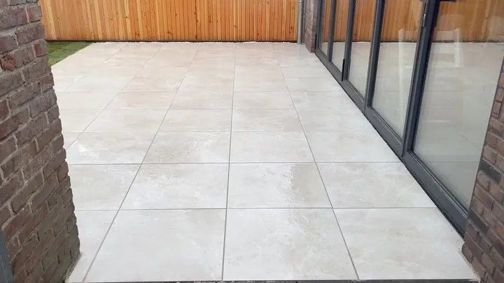 Opgeleverd terras van grote lichte keramische tegels langs een glazen schuifpui