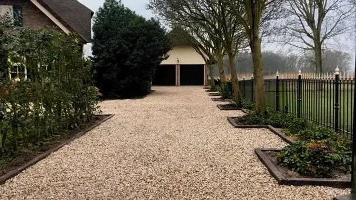 Lange nieuwe oprit van licht grind met kantopsluiting en borders langs een zwart hek