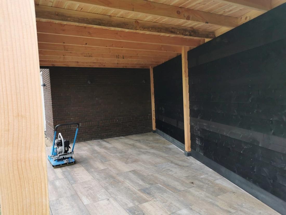 Binnenkant van een overkapping: douglas balken, een zwarte wand en tegels in houtlook