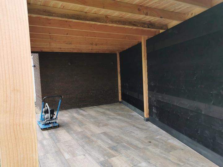 Binnenkant van een overkapping: douglas balken, een zwarte wand en tegels in houtlook