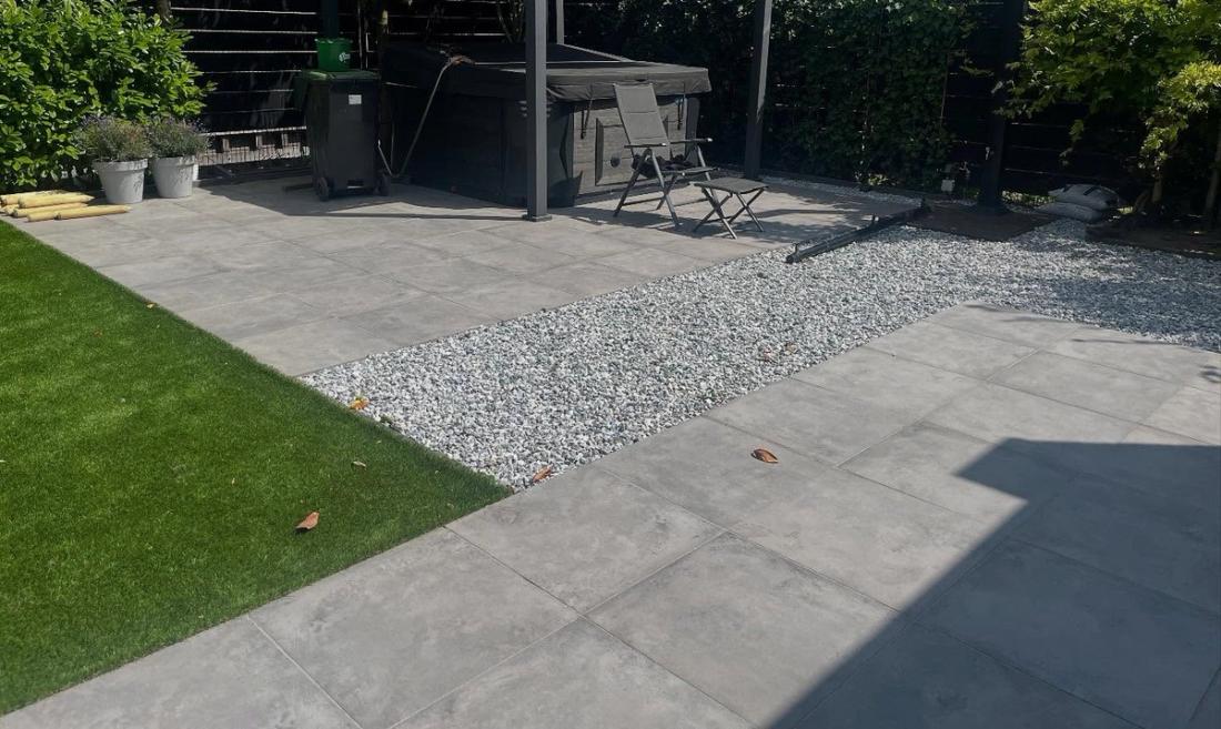 Kunstgras naast een terras van grote grijze tegels en een strook wit grind