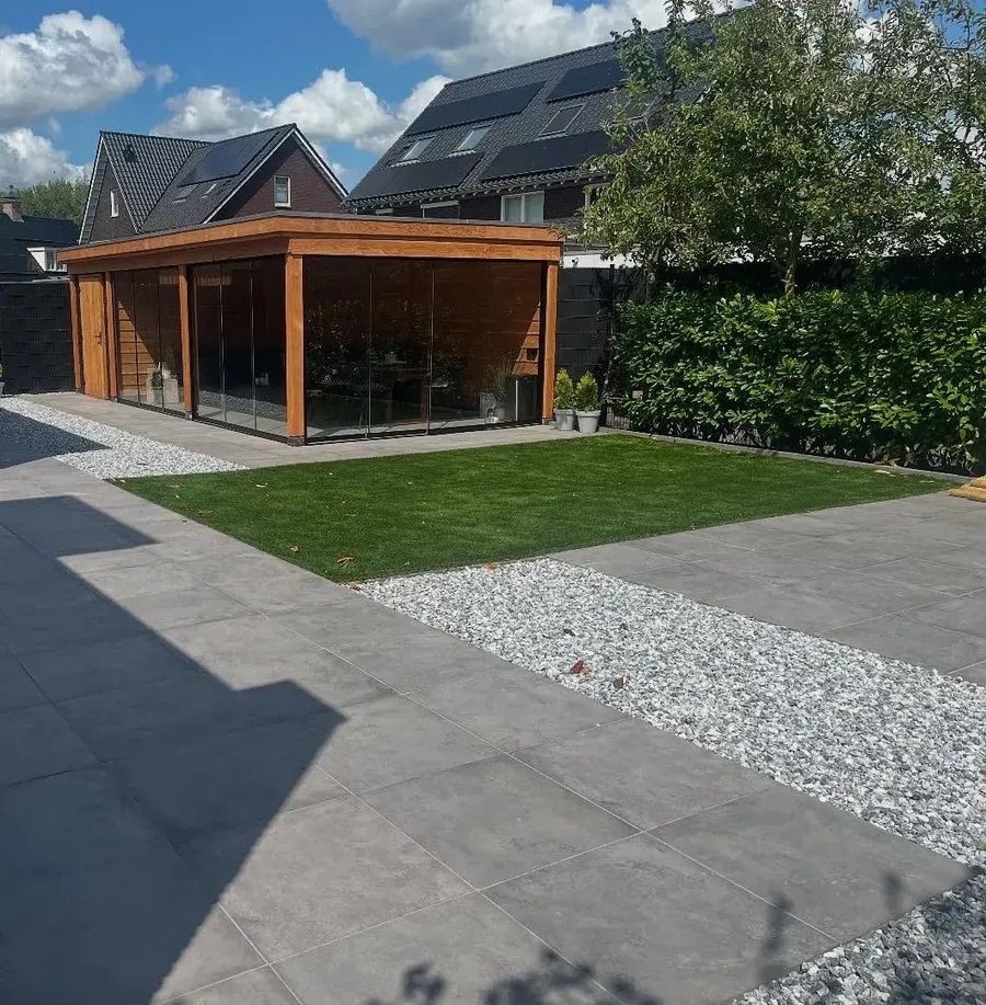 Opgeleverde achtertuin met een terras van grote grijze tegels, een strook wit grind en kunstgras