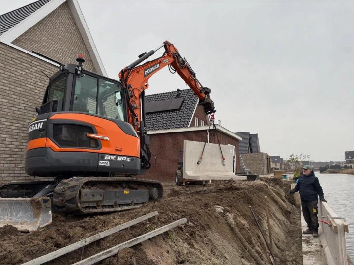 Een minigraver plaatst een betonnen keerwand langs het water in Bergen op Zoom