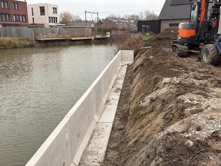 Afgegraven talud langs het water met de nieuwe betonnen keerwand, een graver en een shovel