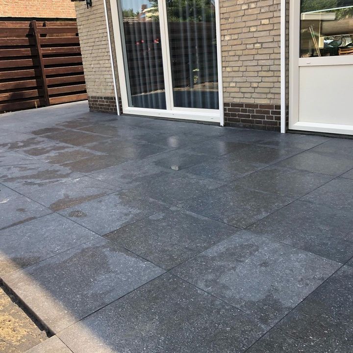 Terras van donkere keramische tegels tegen een achtergevel met schuifpui