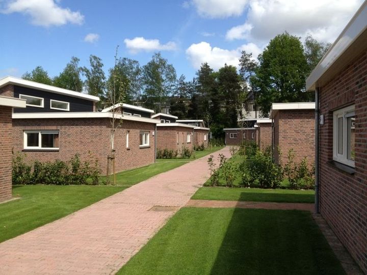 Vakantiepark met bungalows, gemaaide gazons en een pad van rode klinkers