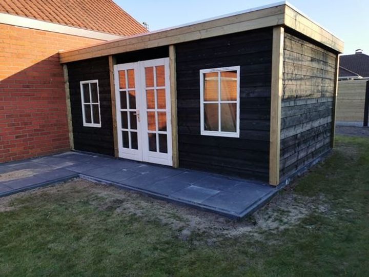 Tuinhuis met een zwarte houten gevel, witte openslaande deuren en ramen