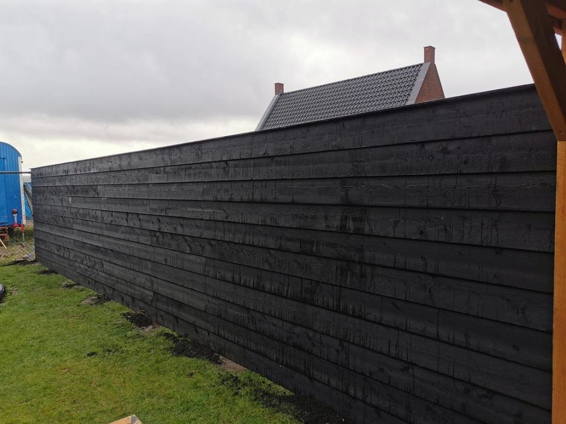 Lange zwarte houten schutting met horizontale planken langs een gazon