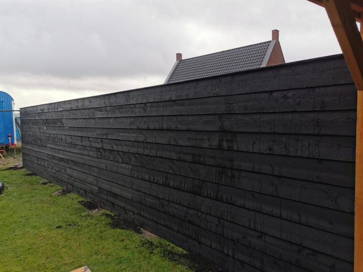 Lange zwarte houten schutting met horizontale planken langs een gazon