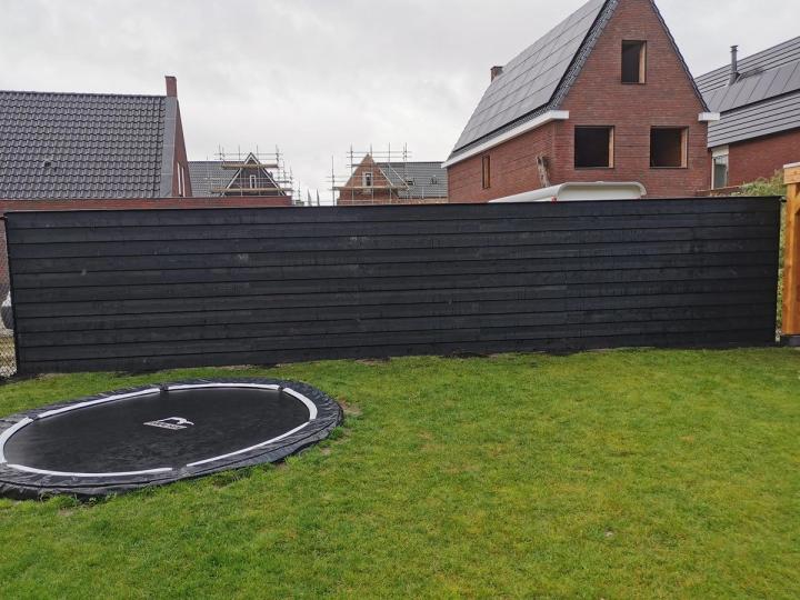 Zwarte schutting langs een gazon met een ingegraven trampoline