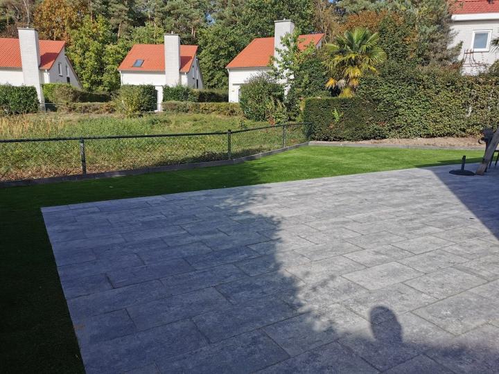 Groot terras van grijze tegels langs een gazon