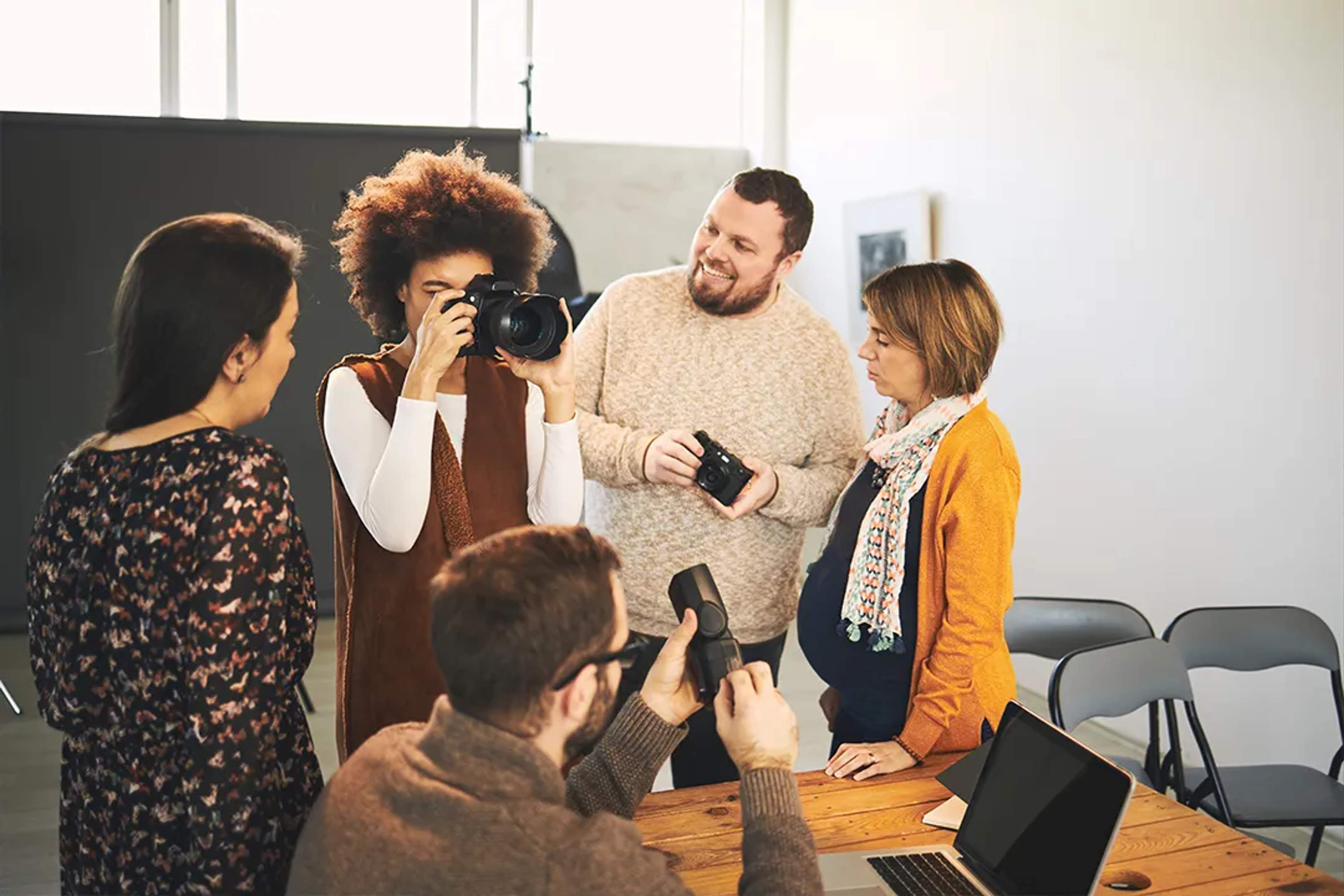Group of people in a photography workshop sharing cameras and learning together indoors.
