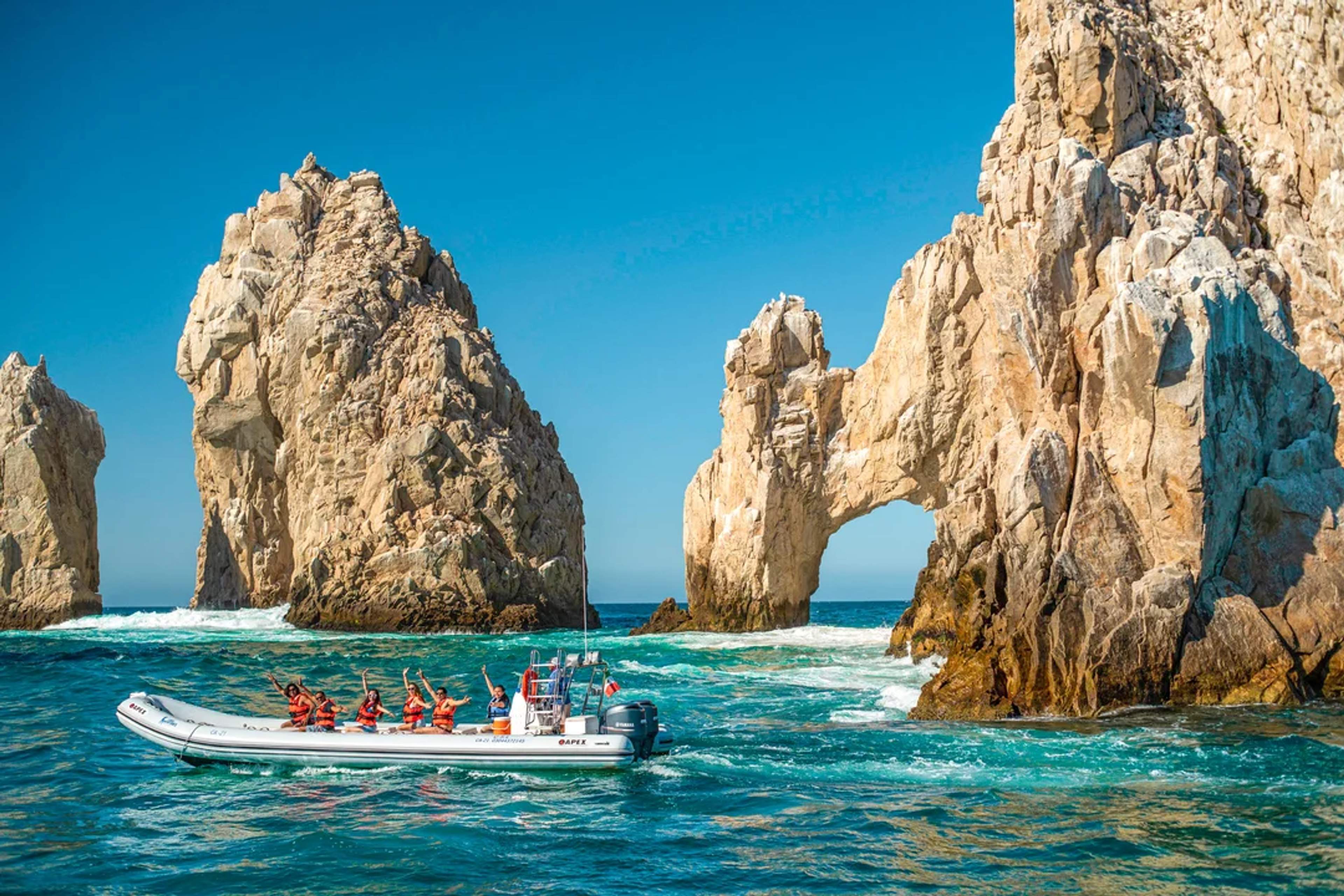 Lancha turística con pasajeros felices cerca de El Arco en Cabo San Lucas en un día soleado.