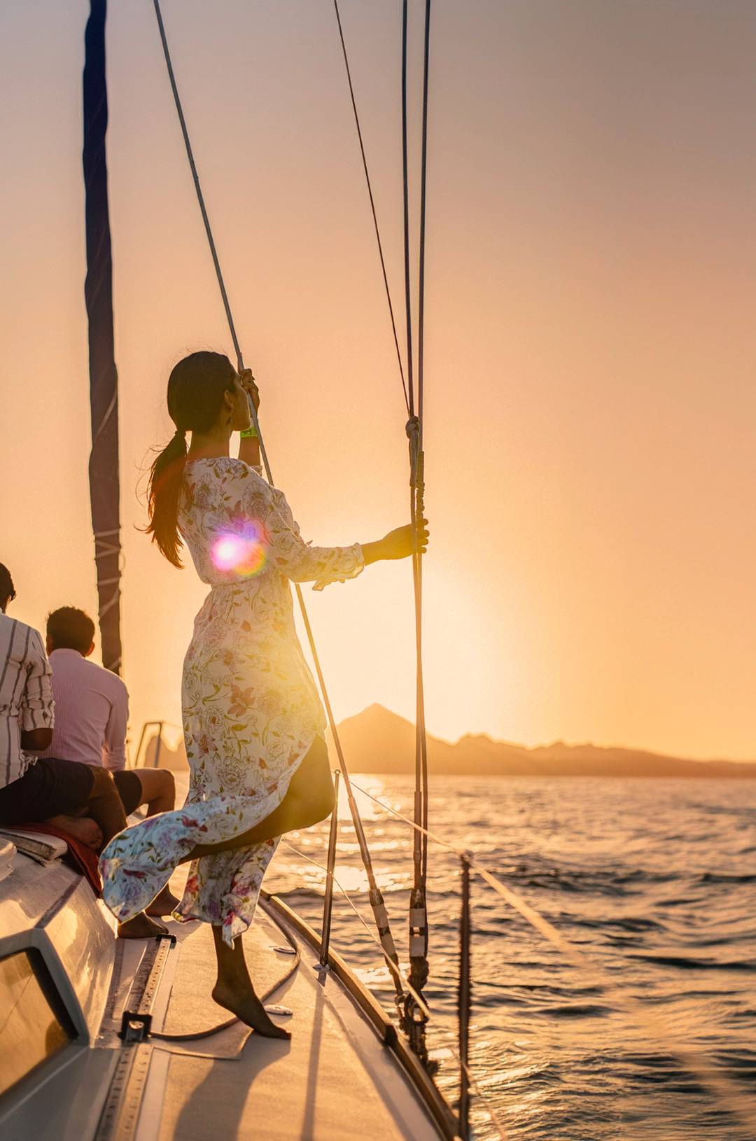 Woman enjoying a sunset view from a sailboat in Cabo, with warm sunlight and ocean waves around her.