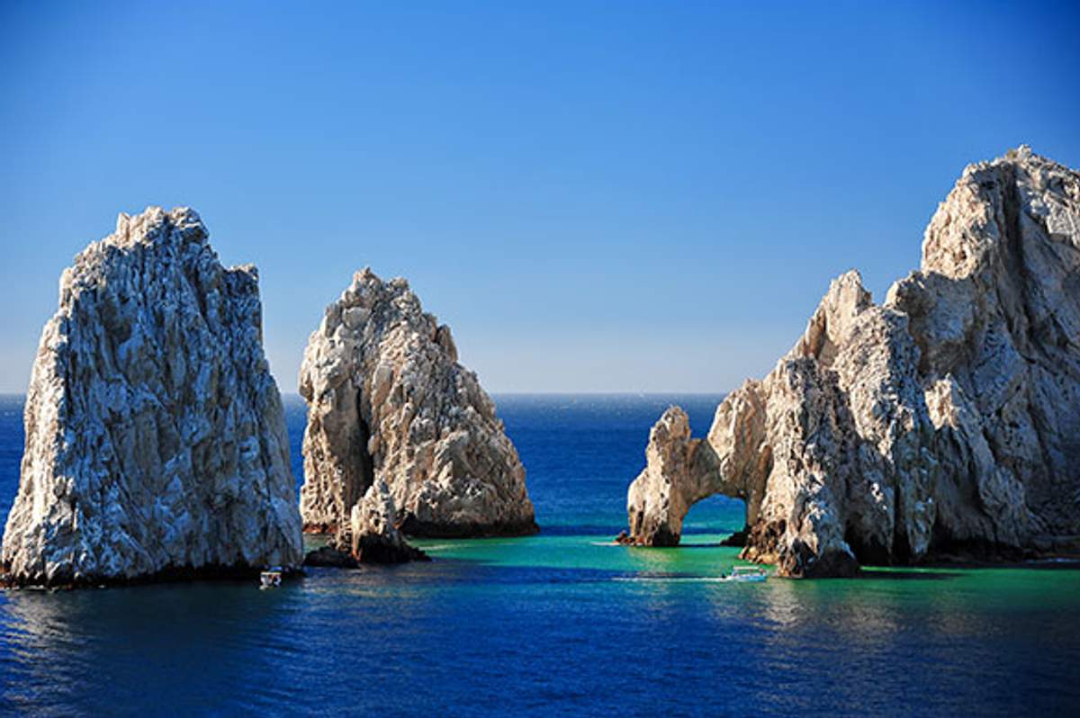 A stunning view of the famous El Arco rock formation in Cabo San Lucas, Mexico, where towering rocky cliffs meet the clear blue ocean, with a small arch visible near the waterline.