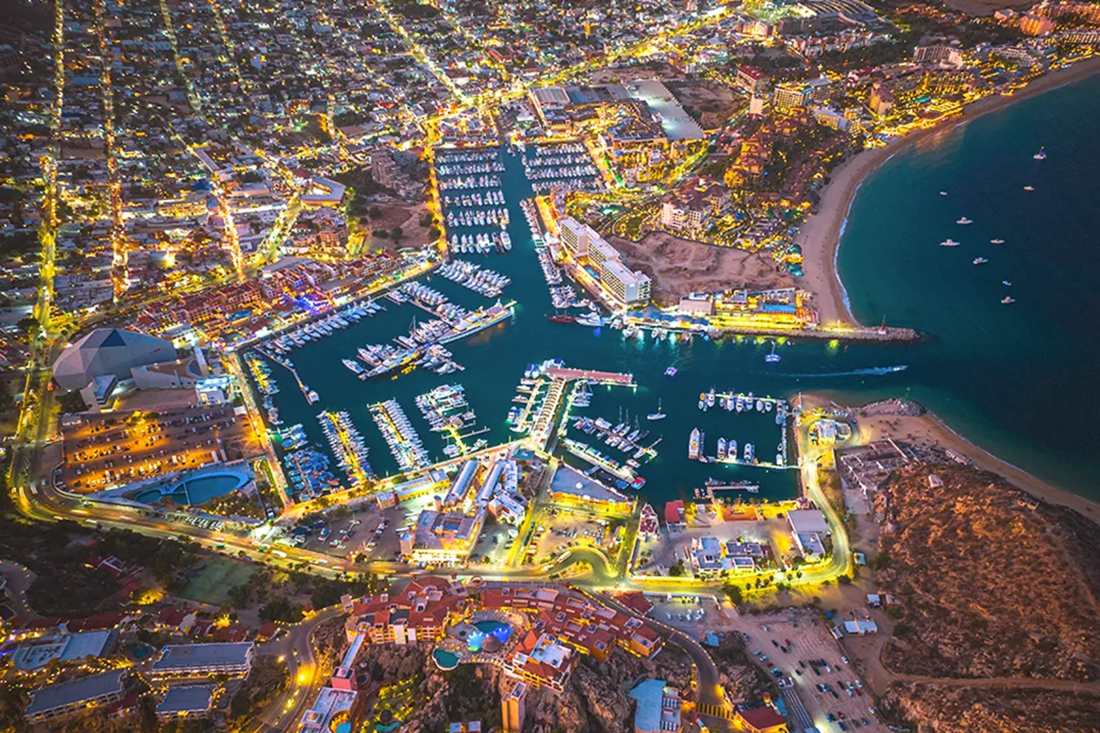 Marina de Cabo San Lucas vista aérea nocturna con puerto iluminado yates y luces vibrantes en Baja California