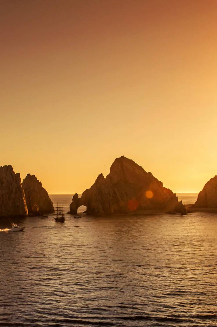 Vista aérea del Arco de Los Cabos con lanchas sobre agua turquesa al atardecer.