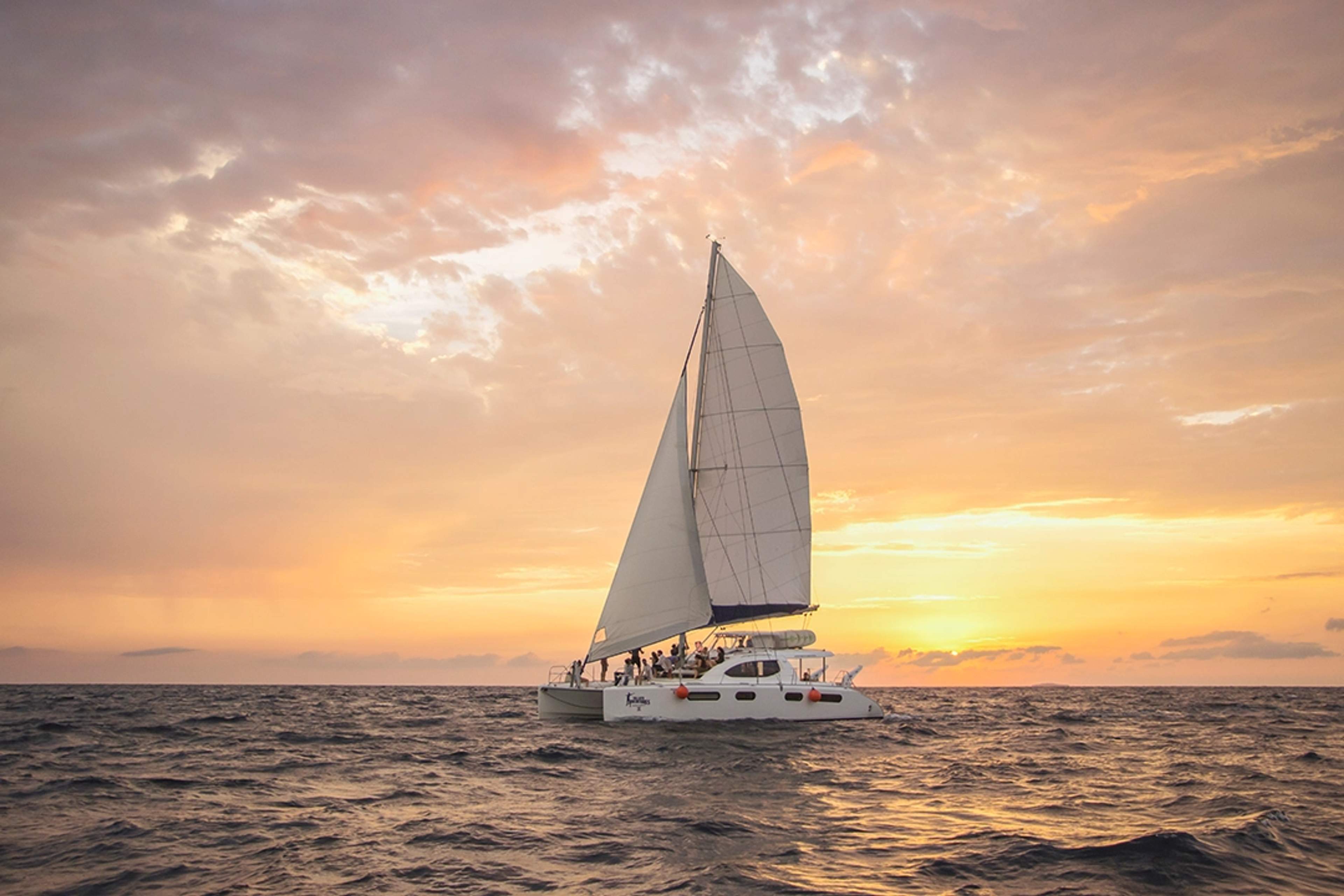 Un velero en el océano al atardecer, con cielos dorados y aguas tranquilas que crean un ambiente sereno.