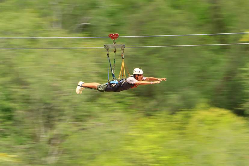 Guest flying Superman-style on a high-speed zipline through lush green jungle during an extreme adventure tour in Mexico