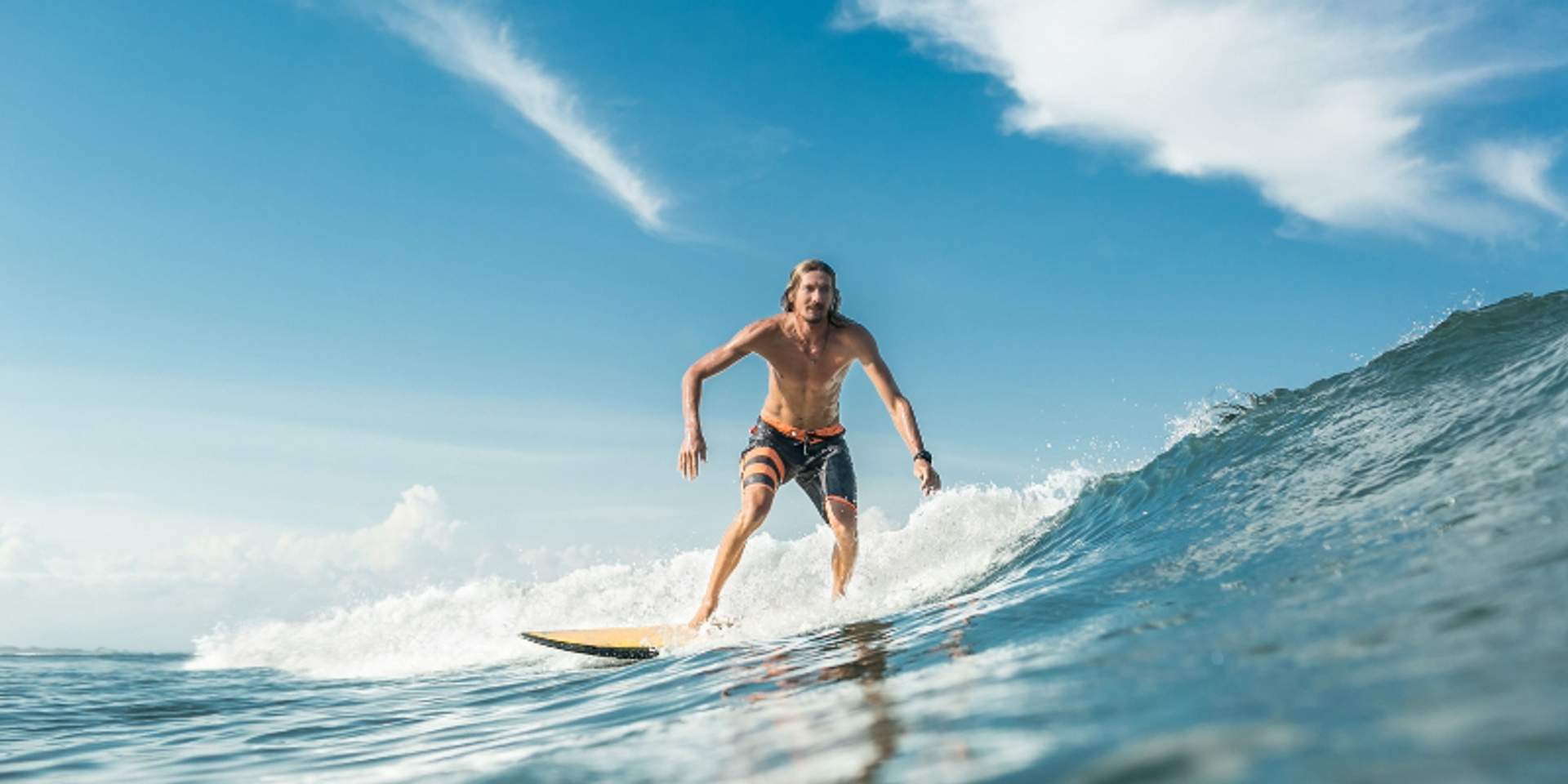 Surfer riding ocean wave under blue sky at Tierra Sagrada Beach & Adventure Park in Cabo