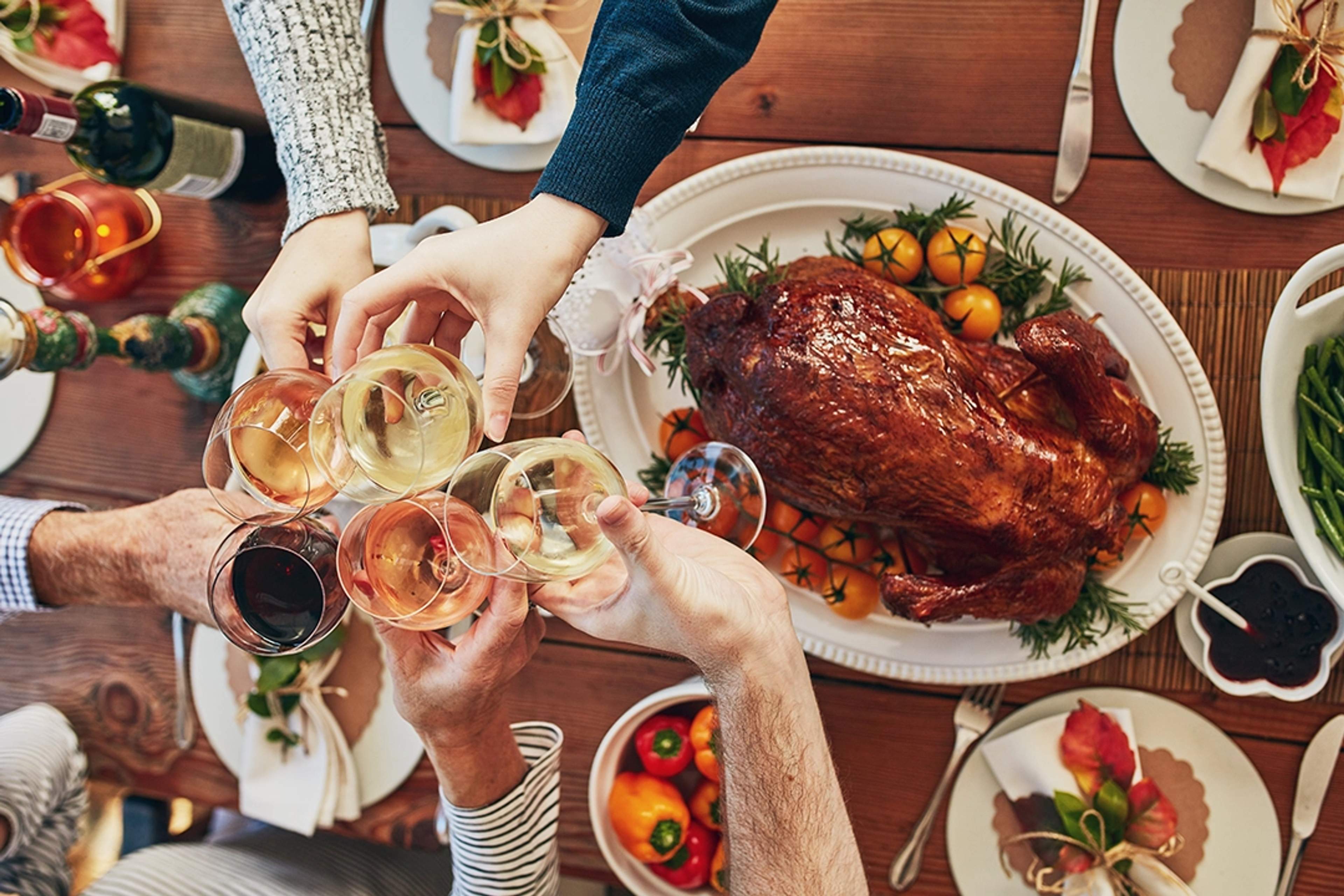Mesa de cena de Thanksgiving con pavo asado, guarniciones y personas brindando con copas de vino.