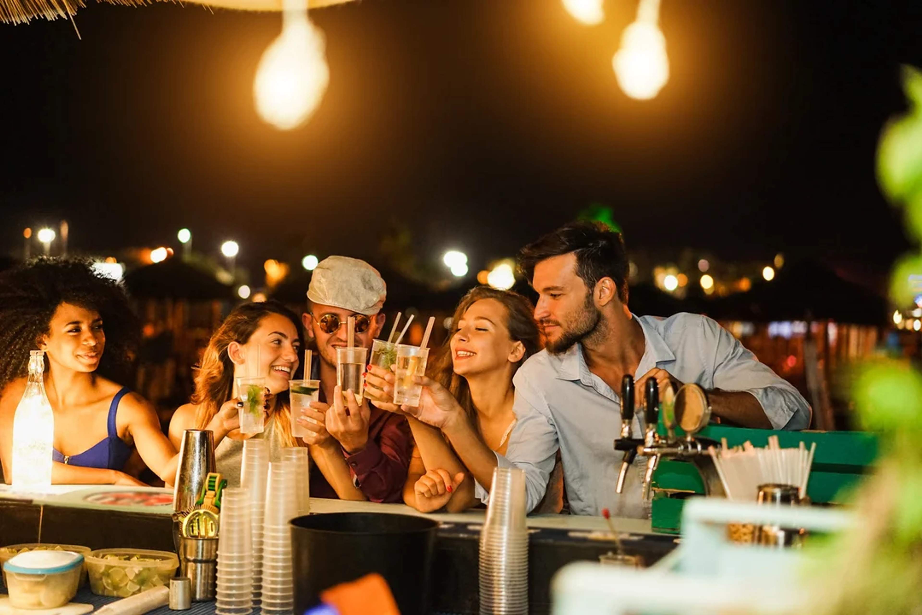 Amigos disfrutan la vida nocturna en Cabo, brindando con cócteles en un animado bar de playa.