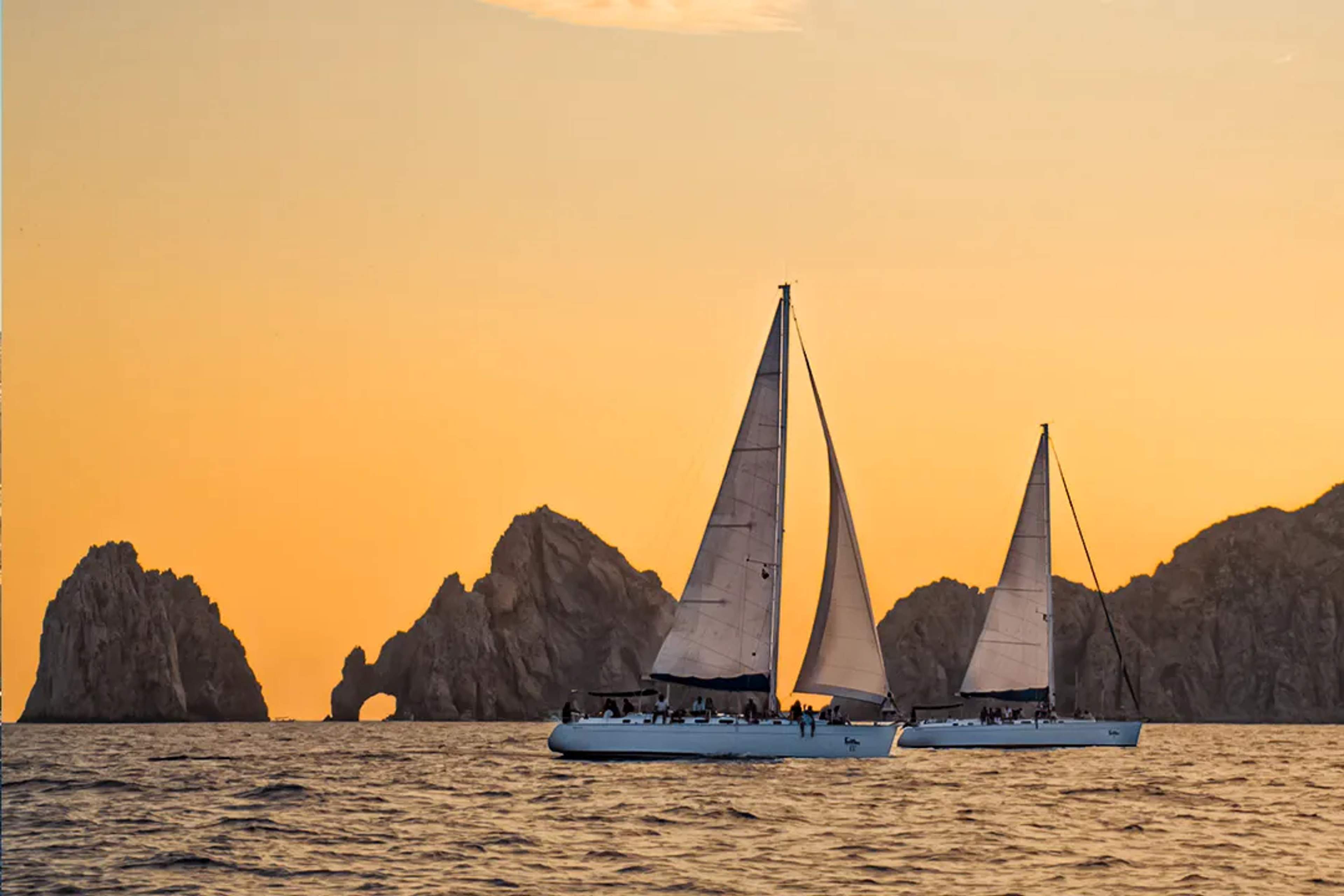 Tour de velero al atardecer en Cabo frente al Arco con yates en silueta y vistas doradas del mar en Baja