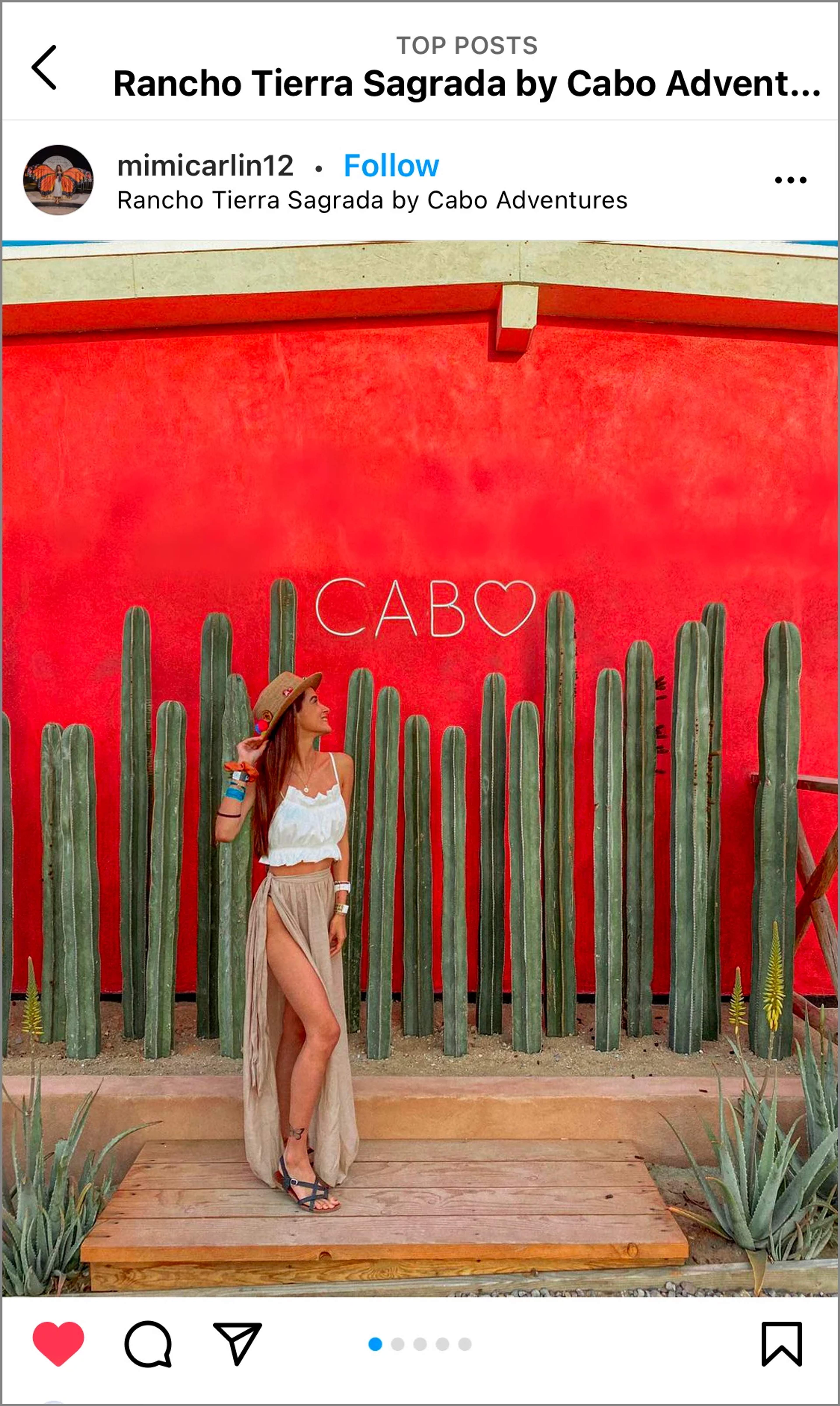 Mujer con sombrero posando junto a un muro rojo con "Cabo" y cactus en Rancho Tierra Sagrada, Cabo Adventures.