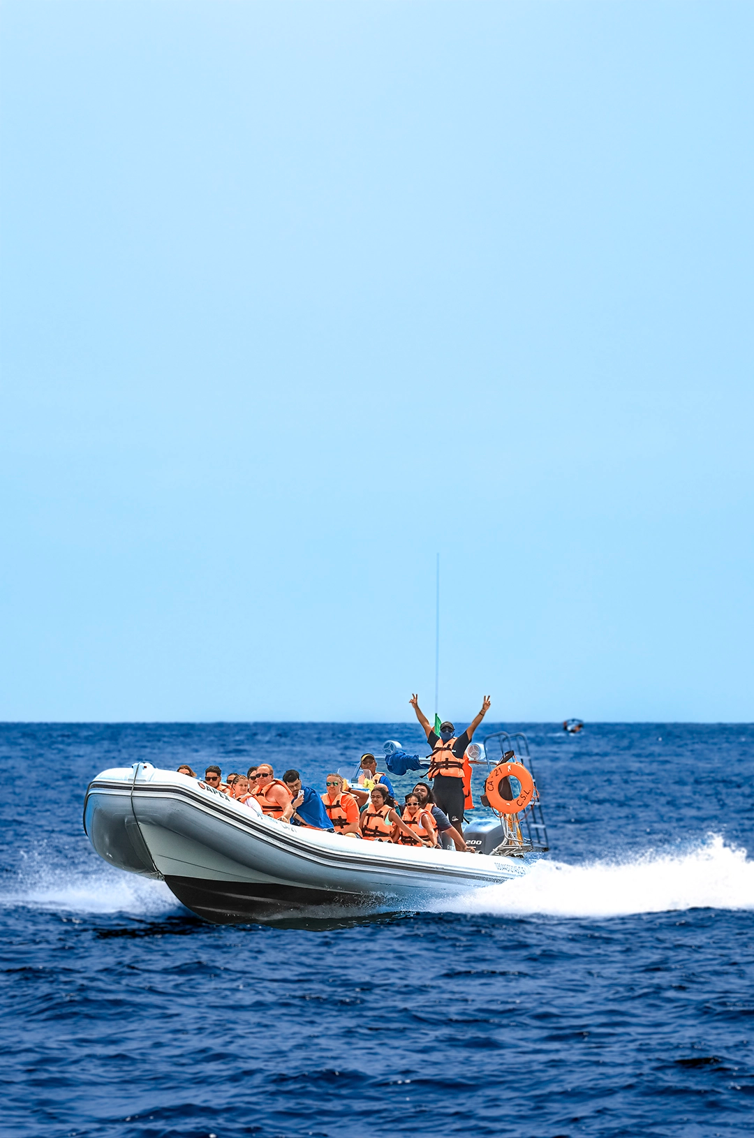Un bote lleno de pasajeros con chalecos naranjas cruza el océano rápidamente, con un guía levantando los brazos emocionado.