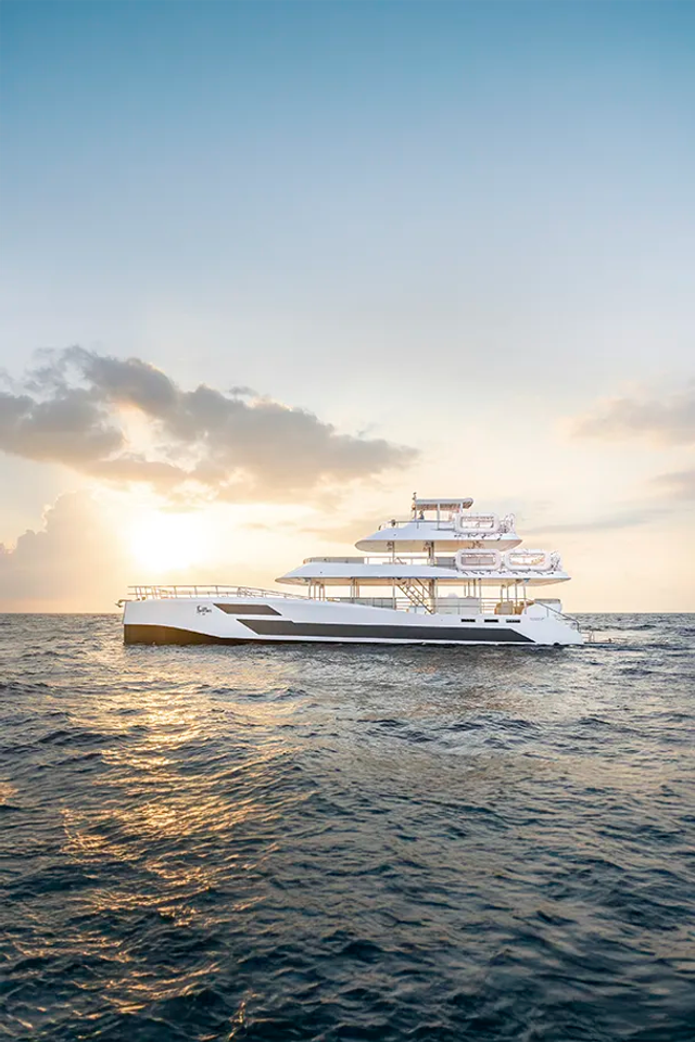 Luxury triple-deck catamaran sailing at sunset on the ocean in Los Cabos.