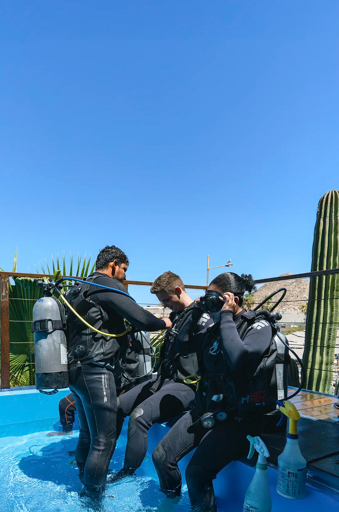 Instructor de buceo ayuda a estudiantes en una alberca en la azotea bajo cielo despejado.