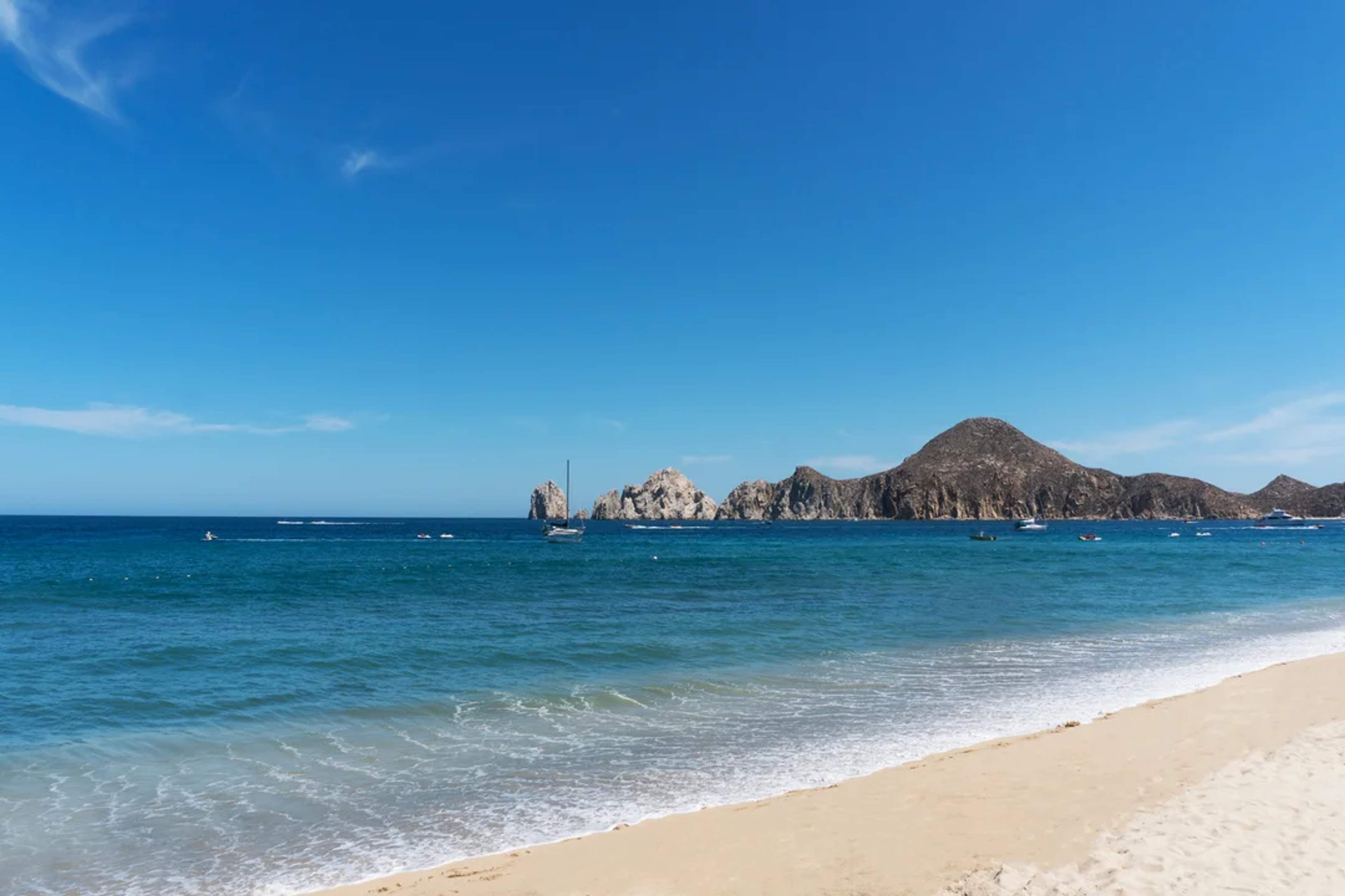 Playa de arena dorada con mar azul y formaciones rocosas icónicas en el fondo.