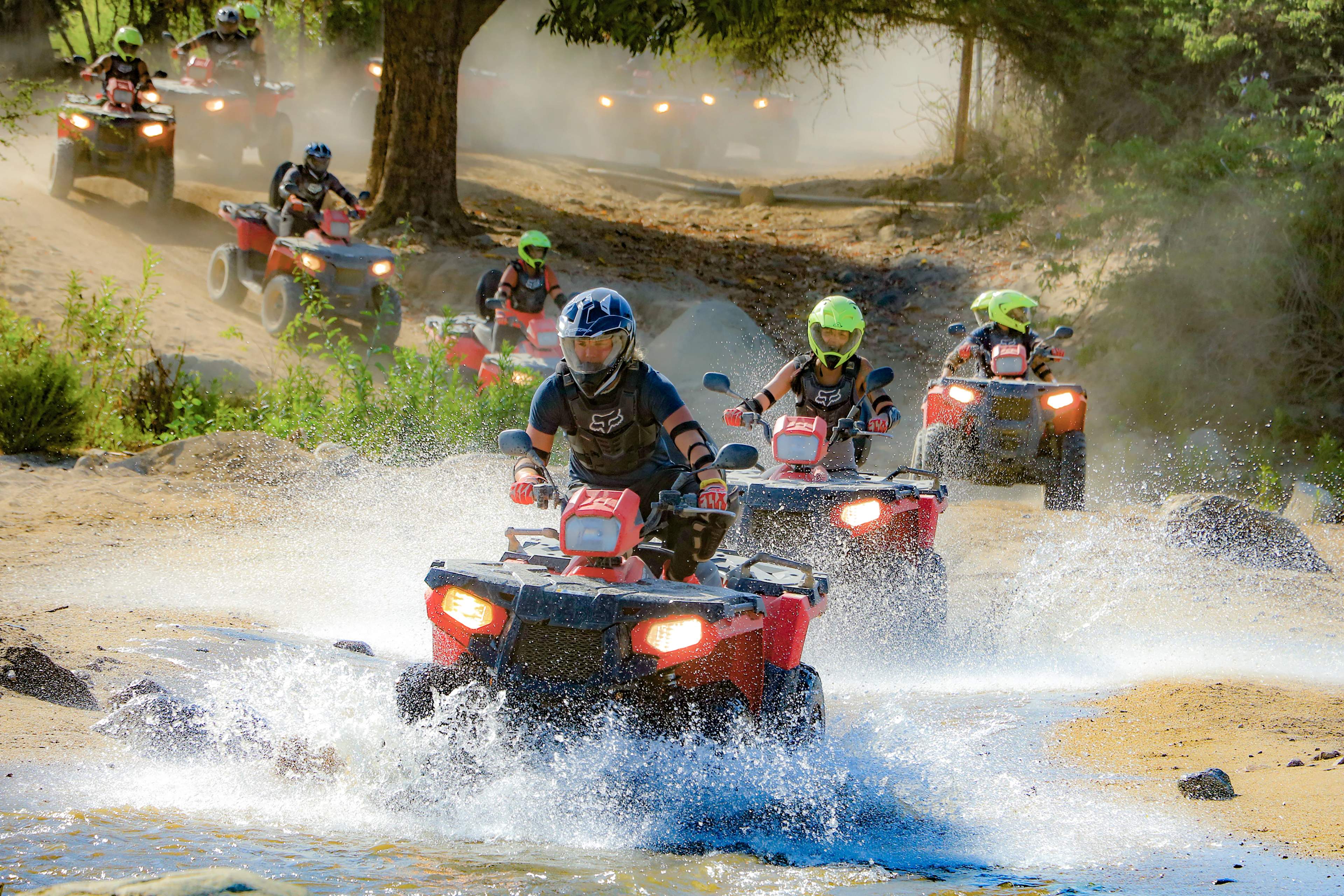 A group of ATV riders splashes through a water crossing on a dusty adventure trail, enjoying the thrill of off-roading.