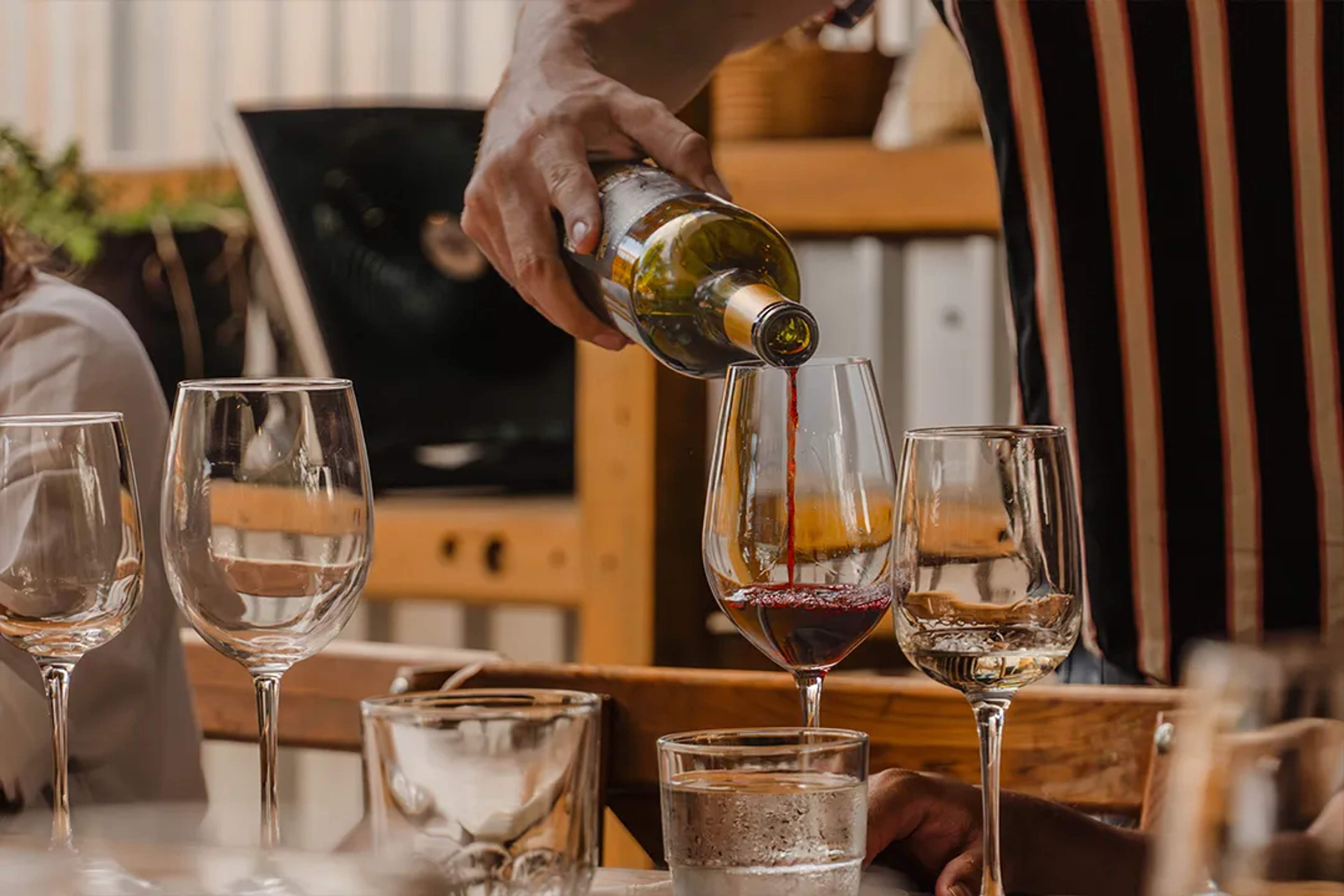 Sommelier pouring red wine during a refined dining experience, with elegant glassware and warm ambiance