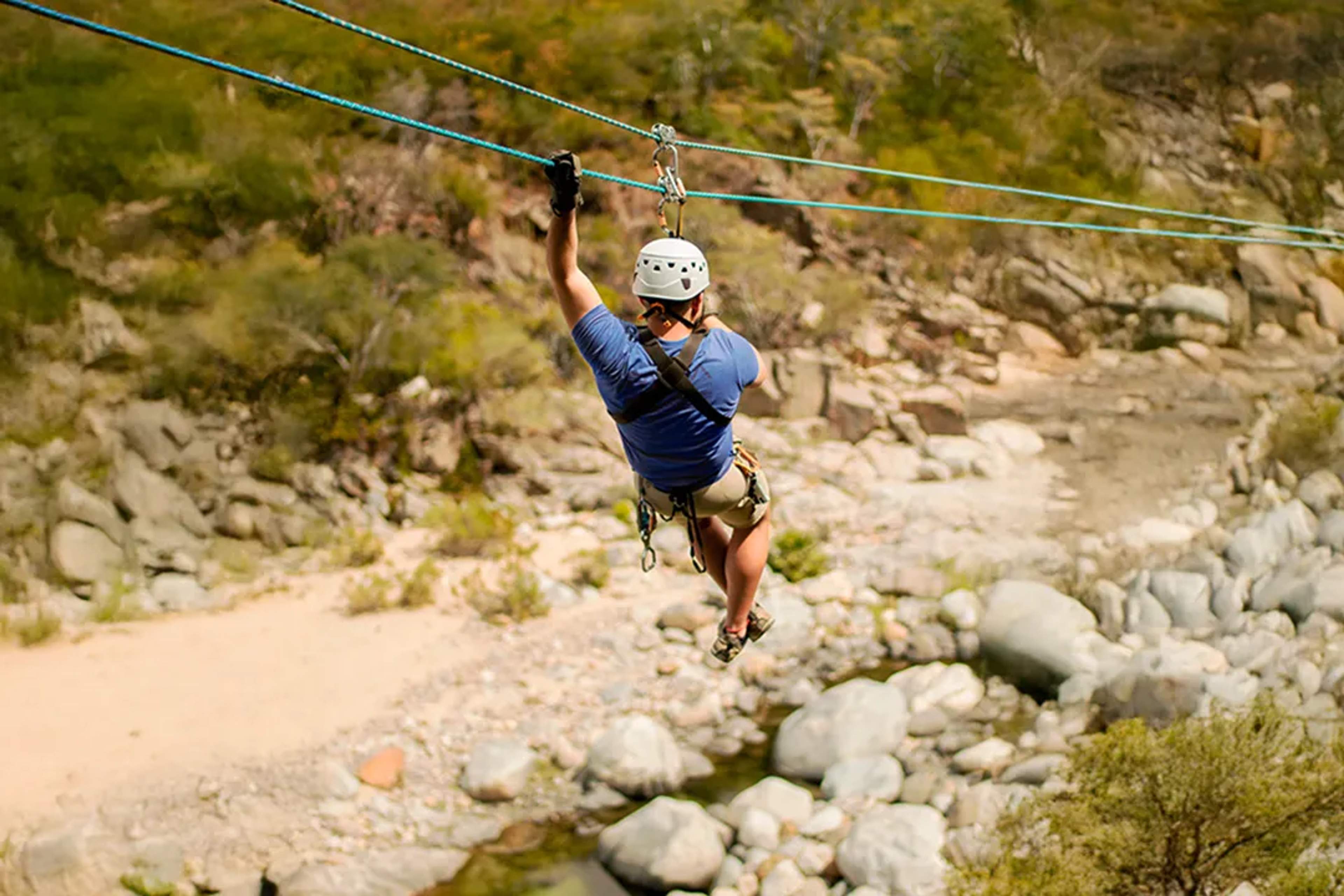 Man ziplining over desert canyon river during Cabo outdoor adventure tour with adrenaline and scenic views.
