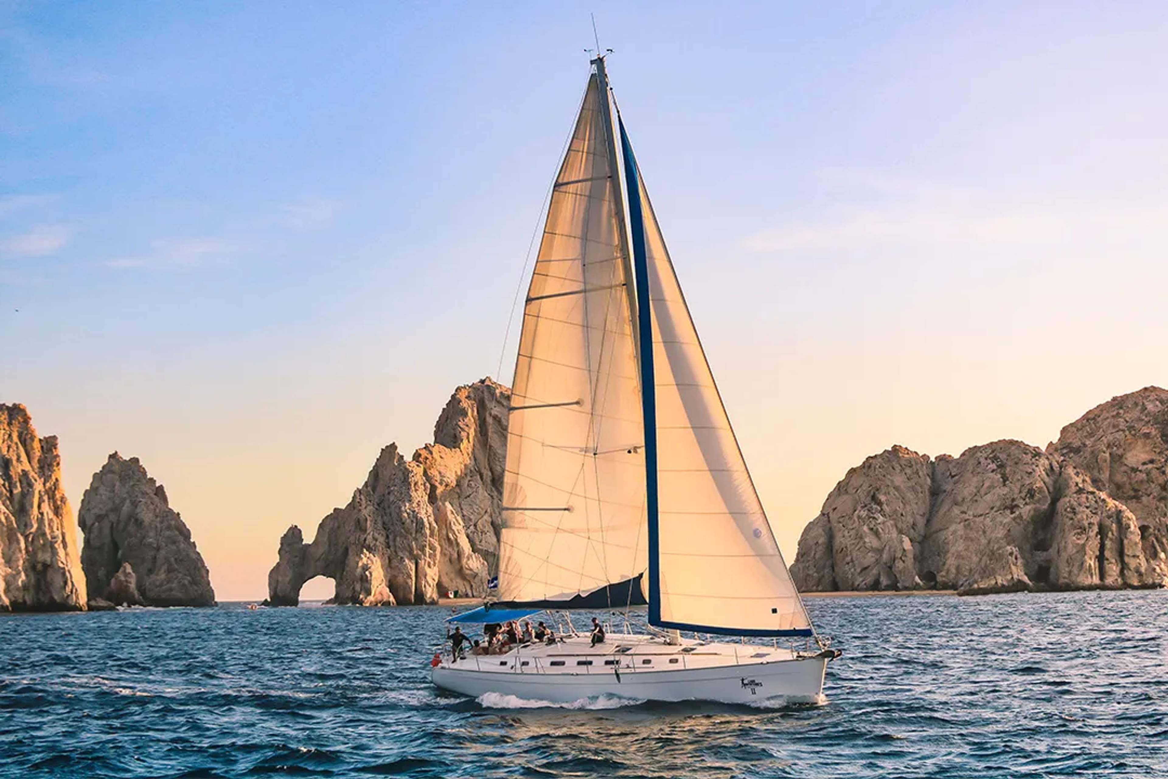 Sailboat cruising at sunset near El Arco in Cabo San Lucas, with golden light, ocean waves and rock formations