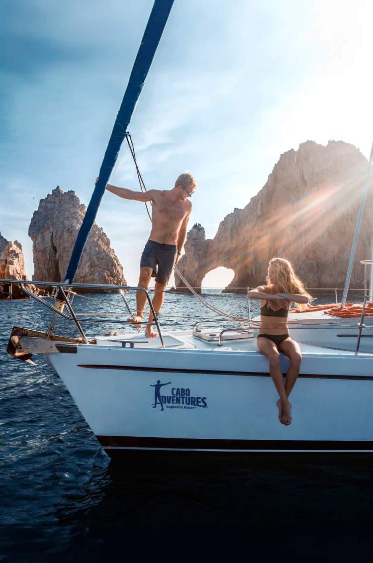 A man and a woman enjoy a sunny day and the view of the Cabo Arch on the best Cabo Sailing tour by Cabo Adventures.
