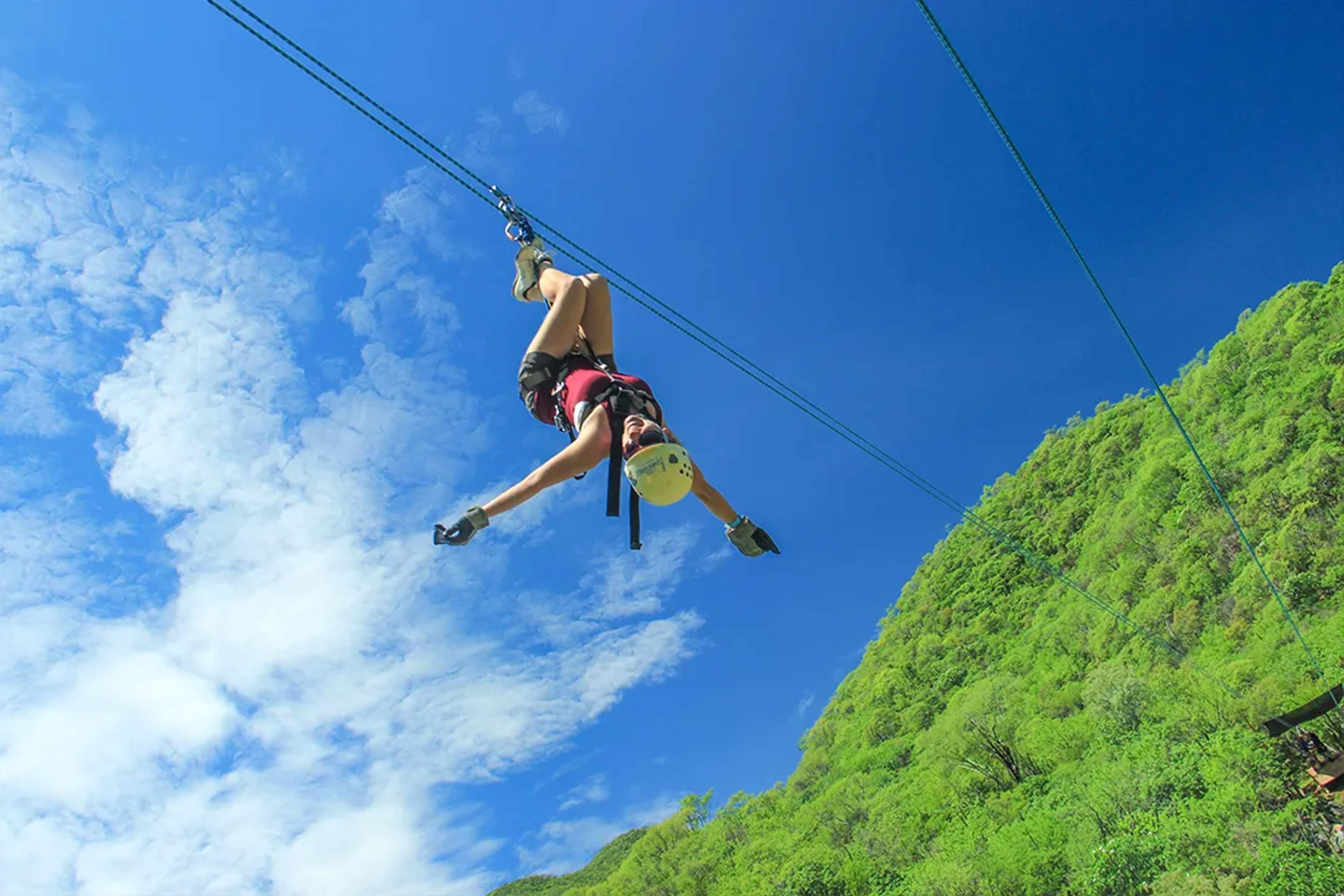 Mujer descendiendo en tirolesa de cabeza sobre la selva verde, viviendo una aventura llena de adrenalina