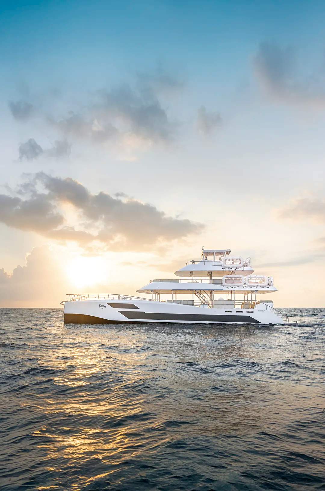 Luxury triple-deck catamaran sailing at sunset on the ocean in Los Cabos.