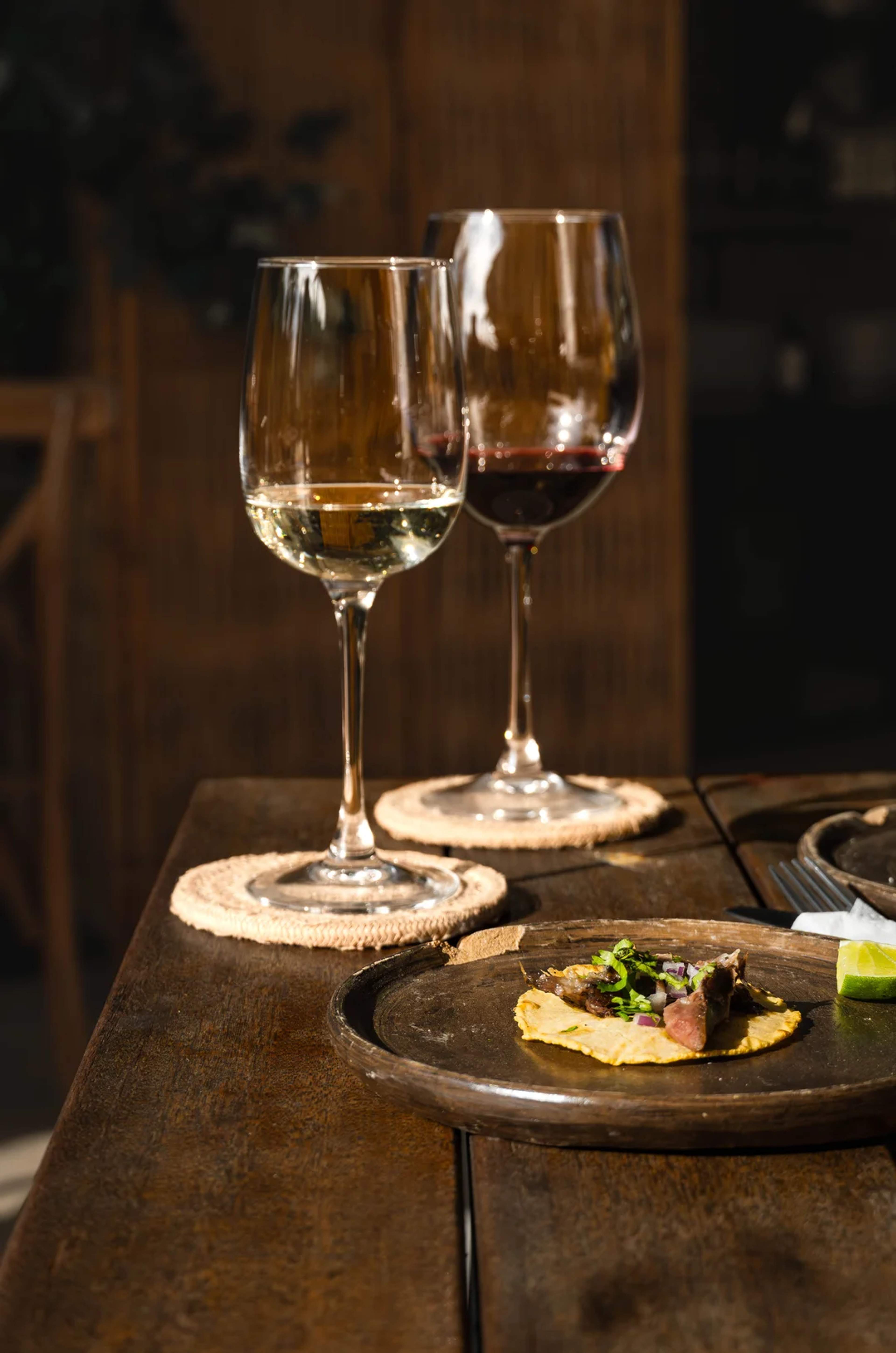Un taco gourmet acompañado de vino tinto y blanco, creando una experiencia culinaria en mesa rústica.
