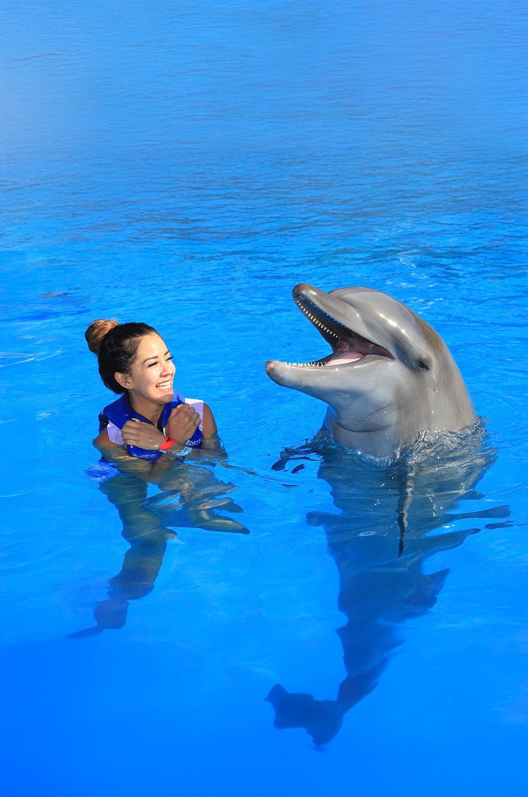 Woman smiles while interacting with a dolphin that appears to be laughing in the water in Cabo San Lucas.
