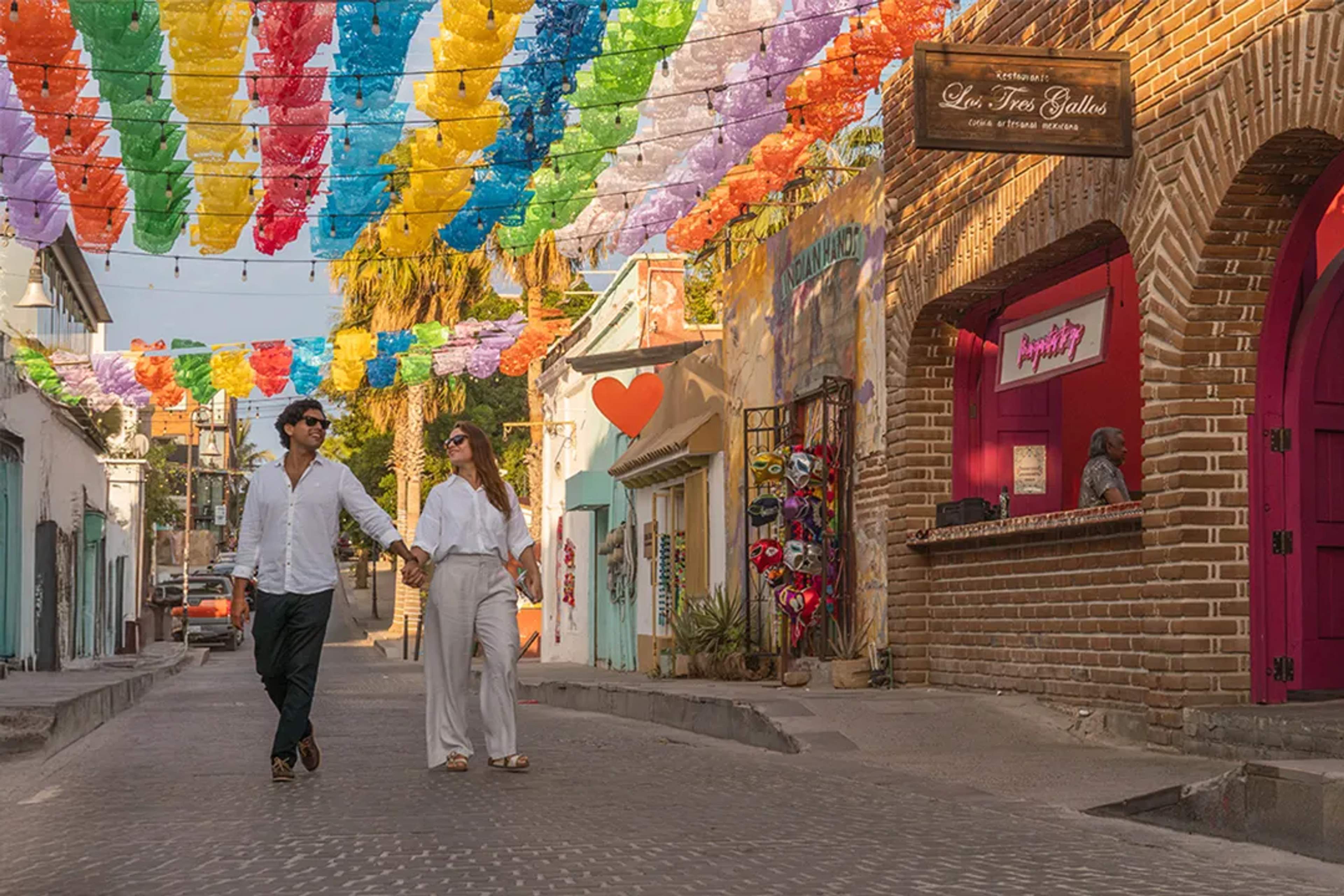 Couple strolling San Jose del Cabo Art Walk with colorful papel picado, galleries and local culture vibes