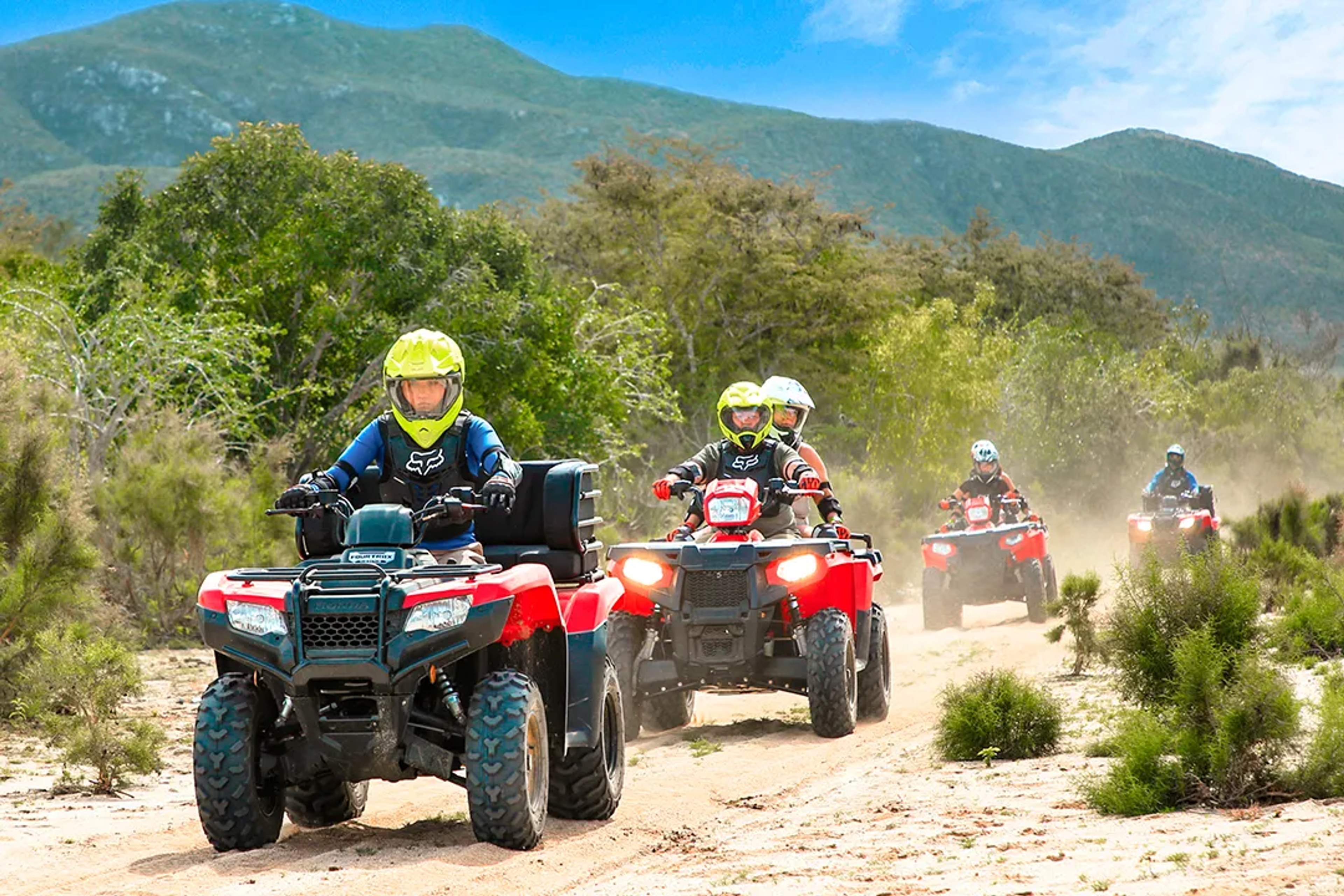 Group riding red ATVs on a dusty trail through the mountains on a sunny adventure day.